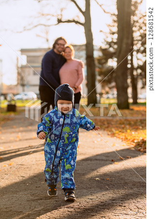 A joyful little boy in his winter coat and hat plays happily in the park, surrounded by the love and warmth of his smiling parents 128681542