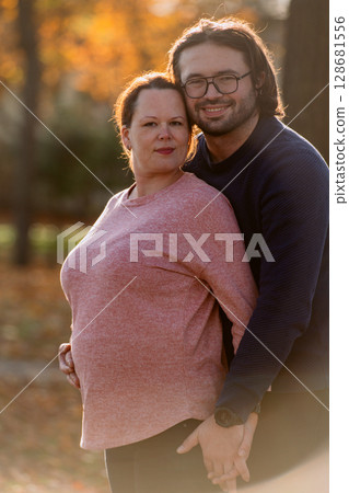 A man lovingly embraces his pregnant wife in the park, sharing a peaceful moment of warmth and affection A man lovingly embraces his pregnant wife in the park, sharing a peaceful moment of warmth and affection 128681556