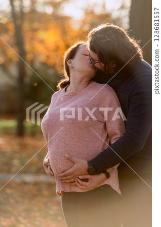 A man lovingly embraces his pregnant wife in the park, sharing a peaceful moment of warmth and affection A man lovingly embraces his pregnant wife in the park, sharing a peaceful moment of warmth and affection 128681557