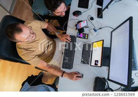 Top view of programmer diligently testing smartphone applications while sitting in their office. 128681569