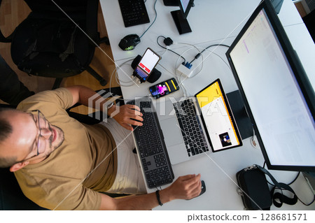 Top view of programmer diligently testing smartphone applications while sitting in their office. 128681571