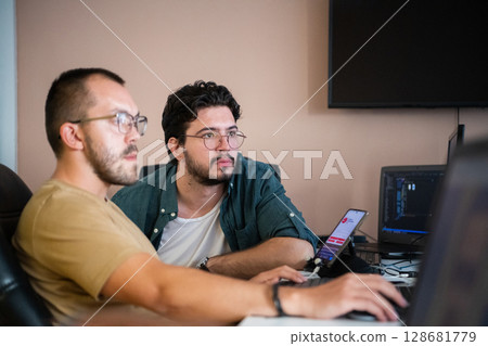 Programmers engrossed in deep collaboration, diligently working together to solve complex problems and develop innovative mobile applications with seamless functionality. 128681779
