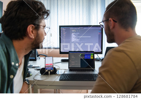 Programmers engrossed in deep collaboration, diligently working together to solve complex problems and develop innovative mobile applications with seamless functionality. 128681784