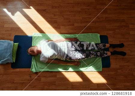 Senior woman practicing stretching and meditation on the floor, focusing on proper alignment and relaxation. 128681918