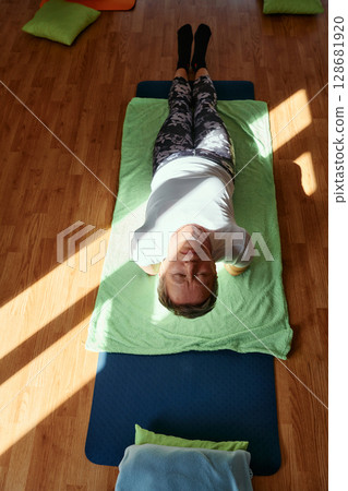 Senior woman practicing stretching and meditation on the floor, focusing on proper alignment and relaxation. 128681920