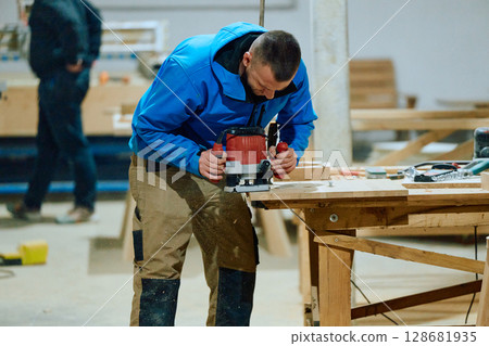 Close Up of Worker Carefully Cutting and Planing Wooden Pieces for Furniture in Wood Industry 128681935