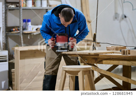 Close Up of Worker Carefully Cutting and Planing Wooden Pieces for Furniture in Wood Industry Close Up of Worker Carefully Cutting and Planing Wooden Pieces for Furniture in Wood Industry 128681945