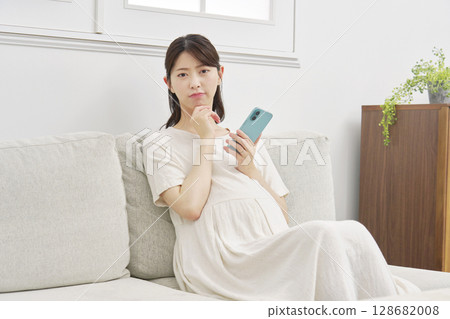Pregnant woman thinking with smartphone in living room 128682008