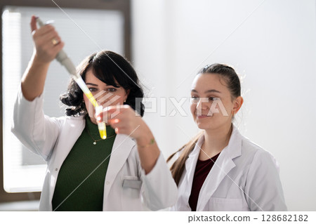 Two scientists holding test tubes with yellow liquid Two scientists holding test tubes with yellow liquid 128682182