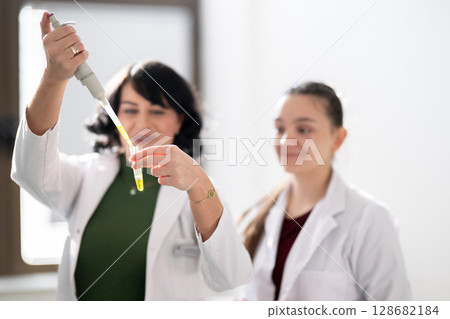Two scientists holding test tubes with yellow liquid Two scientists holding test tubes with yellow liquid 128682184