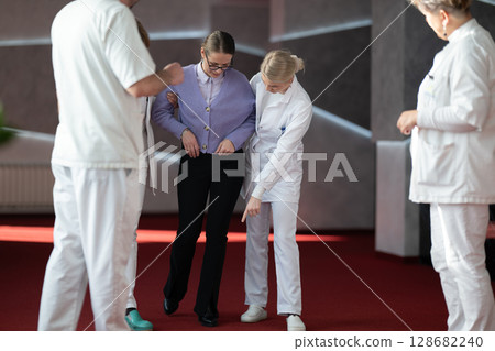 Medical team helping patient with walking therapy 128682240