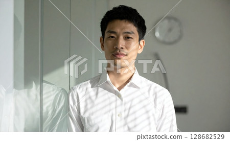 A young businessman in a white shirt shining through the blinds A young businessman in a white shirt shining through the blinds 128682529