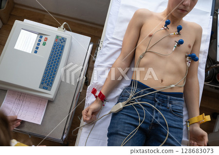A female doctor performs an ECG on a young man in a hospital room, carefully monitoring his heart health during a routine checkup. 128683073