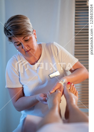 Foot Massage Therapy in a Relaxing Spa Setting. A professional massage therapist in a white uniform provides a soothing foot massage to a client in a calm and serene spa environment 128683084