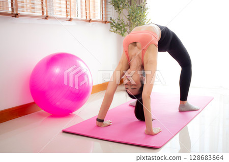 Young asian woman practicing Yoga with stretching muscle back on yoga mat in living room. 128683864