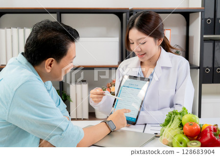 Asian nutritionist using tablet to explaining personalized meal plan with AI to patient. Asian nutritionist using tablet to explaining personalized meal plan with AI to patient. 128683904