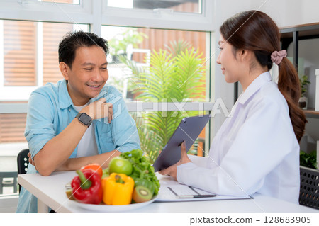 Asian nutritionist using tablet to explaining personalized meal plan with AI to patient. Asian nutritionist using tablet to explaining personalized meal plan with AI to patient. 128683905