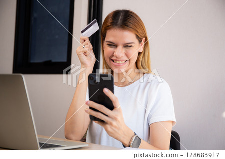 Happy young caucasian woman holding credit card or debit card paying with shopping online. 128683917