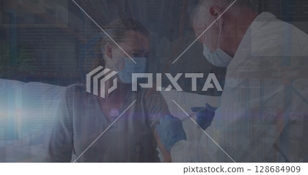 Administering doctor in blue gloves giving vaccine shot on light couch at home, with syringe, masks Administering doctor in blue gloves giving vaccine shot on light couch at home, with syringe, masks 128684909