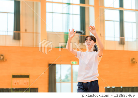 Junior high school and high school girls in gym clothes playing volleyball in a gym Junior high school and high school girls in gym clothes playing volleyball in a gym 128685469