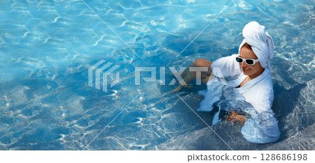A girl in a white coat swims in a blue pool. Wearing sunglasses and a towel. Epilation of legs, varicose veins. Rest, relaxation on the beach, at the hotel. A woman in freedom. Vacation. High quality 128686198
