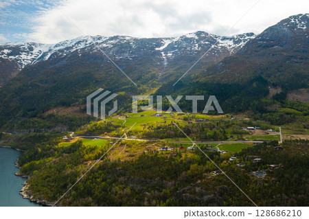 Hardanger Bridge gracefully spans vast body of fjord with towering mountains forming dramatic backdrop. Modern suspension bridge with prominent towers Hardanger Bridge gracefully spans vast body of fjord with towering mountains forming dramatic backdrop. Modern suspension bridge with prominent towers 128686210