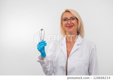 Portrait of confident female dentist with gloves and instruments, ready for dental procedure. Healthcare, clinic and professional care concept Portrait of confident female dentist with gloves and instruments, ready for dental procedure. Healthcare, clinic and professional care concept 128686214