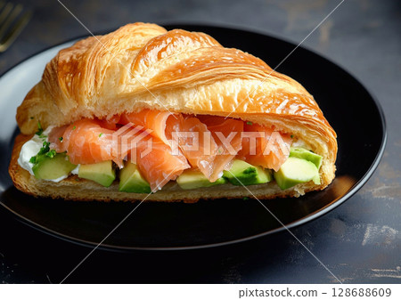 Croissant salmon sandwich with creamy cheese and and fresh avocado on black plate.AI Generative. 128688609