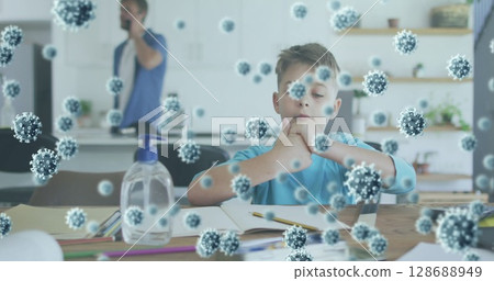 Studying boy coloring homework at home kitchen with notebook, pencils, sanitizer and virus overlay 128688949