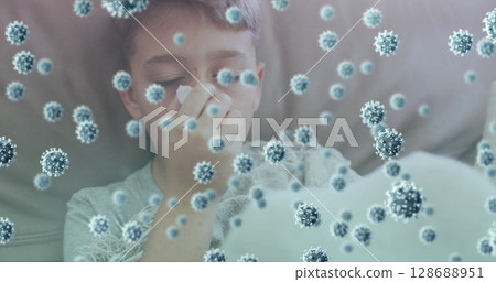 Blowing nose boy reclining on sofa in living room, with tissue blanket and virus graphics 128688951