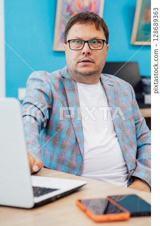 Business man with glasses at desk with laptop in office Business man with glasses at desk with laptop in office 128689363