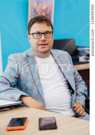 Business man with glasses at desk with laptop in office Business man with glasses at desk with laptop in office 128689366