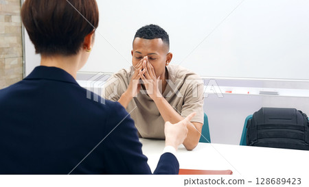 A Japanese female staff member interviewing a troubled black man A Japanese female staff member interviewing a troubled black man 128689423