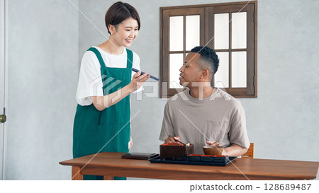 一名餐廳員工使用智慧型手機上的翻譯應用程式為一名黑人男子提供服務 一名餐廳員工使用智慧型手機上的翻譯應用程式為一名黑人男子提供服務 128689487