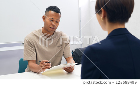 一名黑人男子和一名日本女工作人員簽署文件 一名黑人男子和一名日本女工作人員簽署文件 128689499