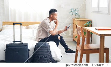 Black male traveler looking at smartphone in hotel room 128689505