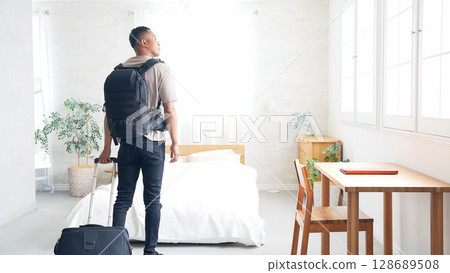 黑人男性旅人提著行李箱站在飯店房間裡 黑人男性旅人提著行李箱站在飯店房間裡 128689508