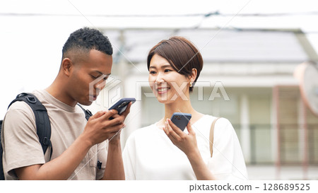 一名日本女性正在使用智慧型手機翻譯應用程式與一名黑人男子交談 128689525