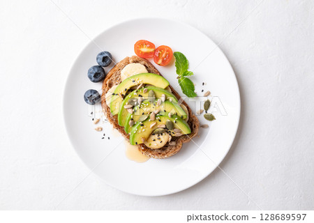 Avocado toast with banana, sunflower seed, pumpkin seeds, sesame seeds, blueberry, tomato and honey 128689597