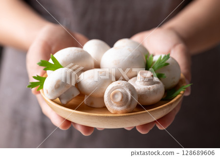 White Button mushroom or Champignon mushroom (Agaricus bisporus) on wooden plate holding by hand White Button mushroom or Champignon mushroom (Agaricus bisporus) on wooden plate holding by hand 128689606