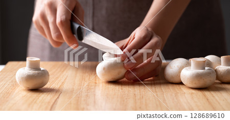 Hand holding kitchen knife and cutting white Button mushroom or Champignon mushroom on wooden board 128689610