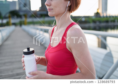 Woman resting after her morning workout, drinking water on a city bridge 128689793