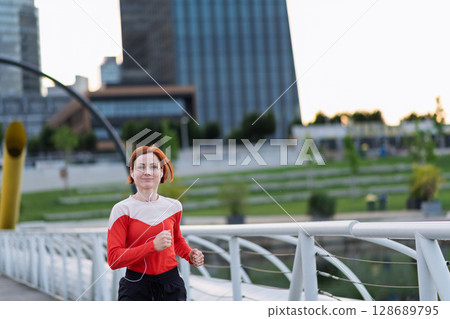 sporty woman running across a city bridge during her morning workout. 128689795