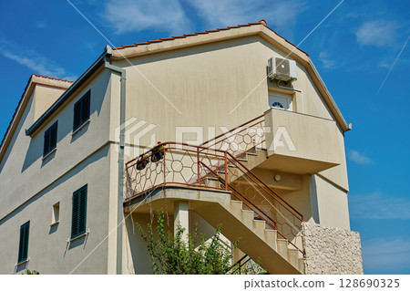 Traditional Mediterranean house with stone walls and green shutters against blue sky. Traditional residential architecture in coastal town 128690325