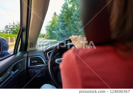Rear view of woman holding steering wheel while driving on sunny road. Female driver in vehicle. Concept of freedom, travel and road trip Rear view of woman holding steering wheel while driving on sunny road. Female driver in vehicle. Concept of freedom, travel and road trip 128690367