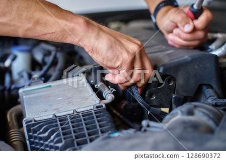 Close-up view of mechanic using ratchet tool to repair car engine under open hood. Auto service, car maintenance and technical repair 128690372