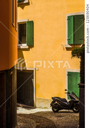 Yellow stucco wall with green shutters and parked scooter in Italian alley at noon. High quality photo 128690404