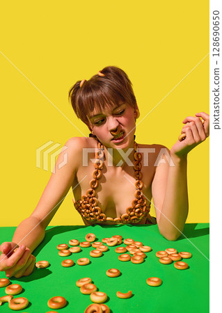 Grumpy woman grimacing while surrounded by scattered ring snacks on green table 128690650