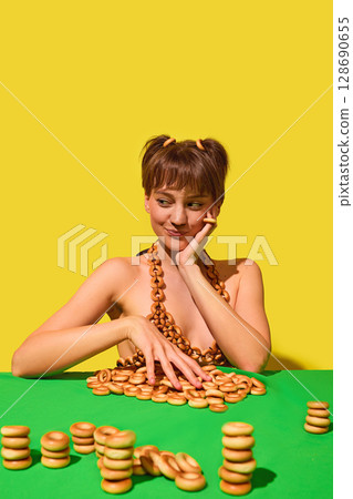 Smirking woman arranging ring snacks on table wearing playful bagel bikini 128690655