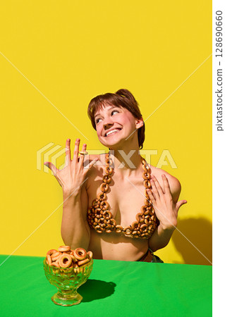 Playful woman showing off bread rings top with smiling expression and yellow background Playful woman showing off bread rings top with smiling expression and yellow background 128690660